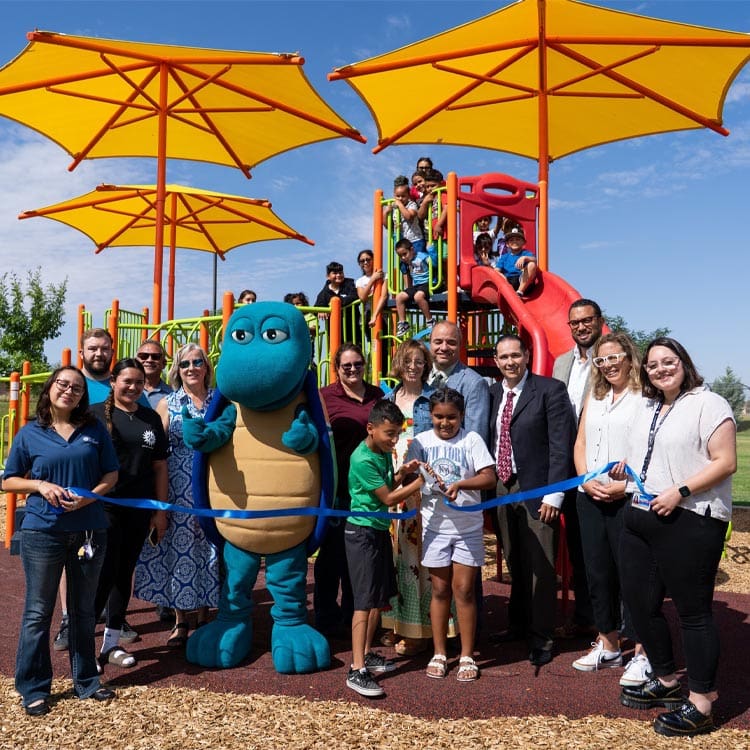 kids cutting a ribbon in front of a new playground alongside city Administrators.