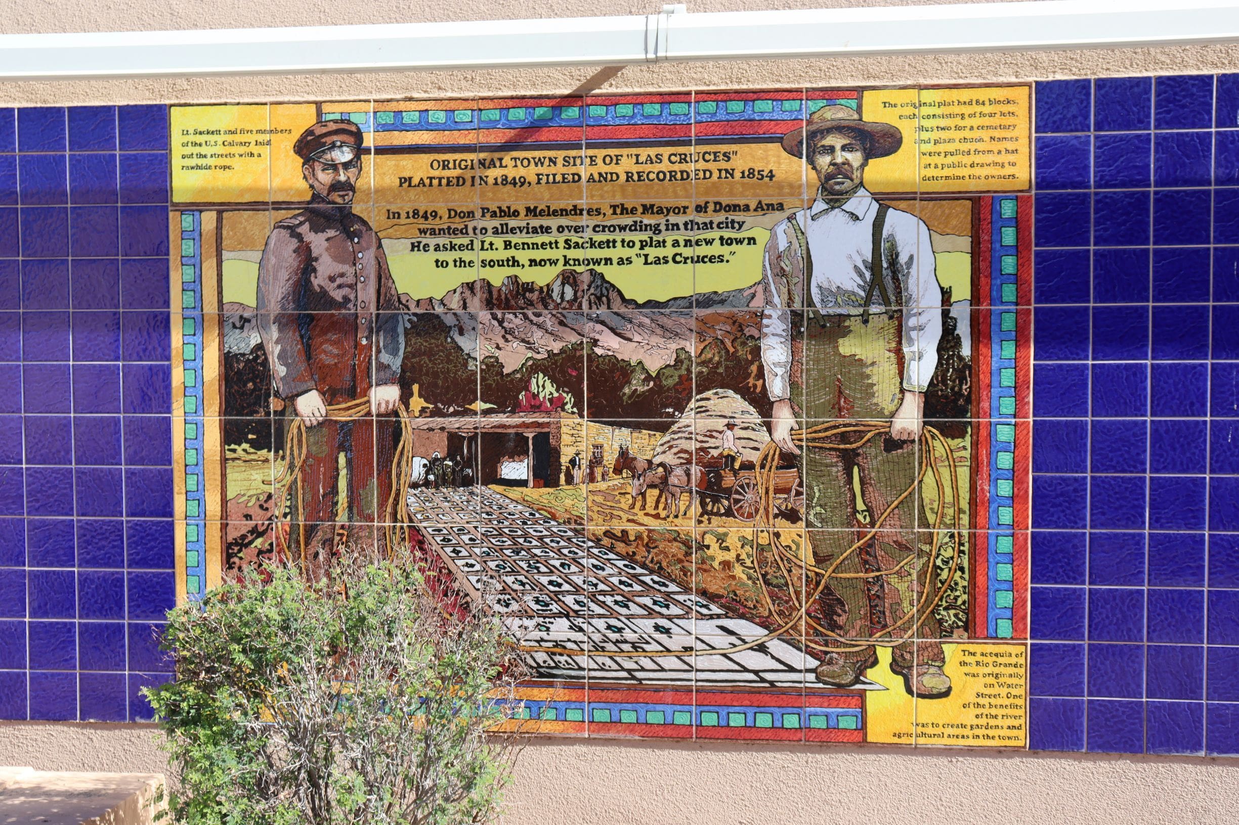 Mosaic mural of two men standing near layout of squares depicting the original townsite