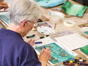 Woman painting on a table with oil paint tubes scattered.