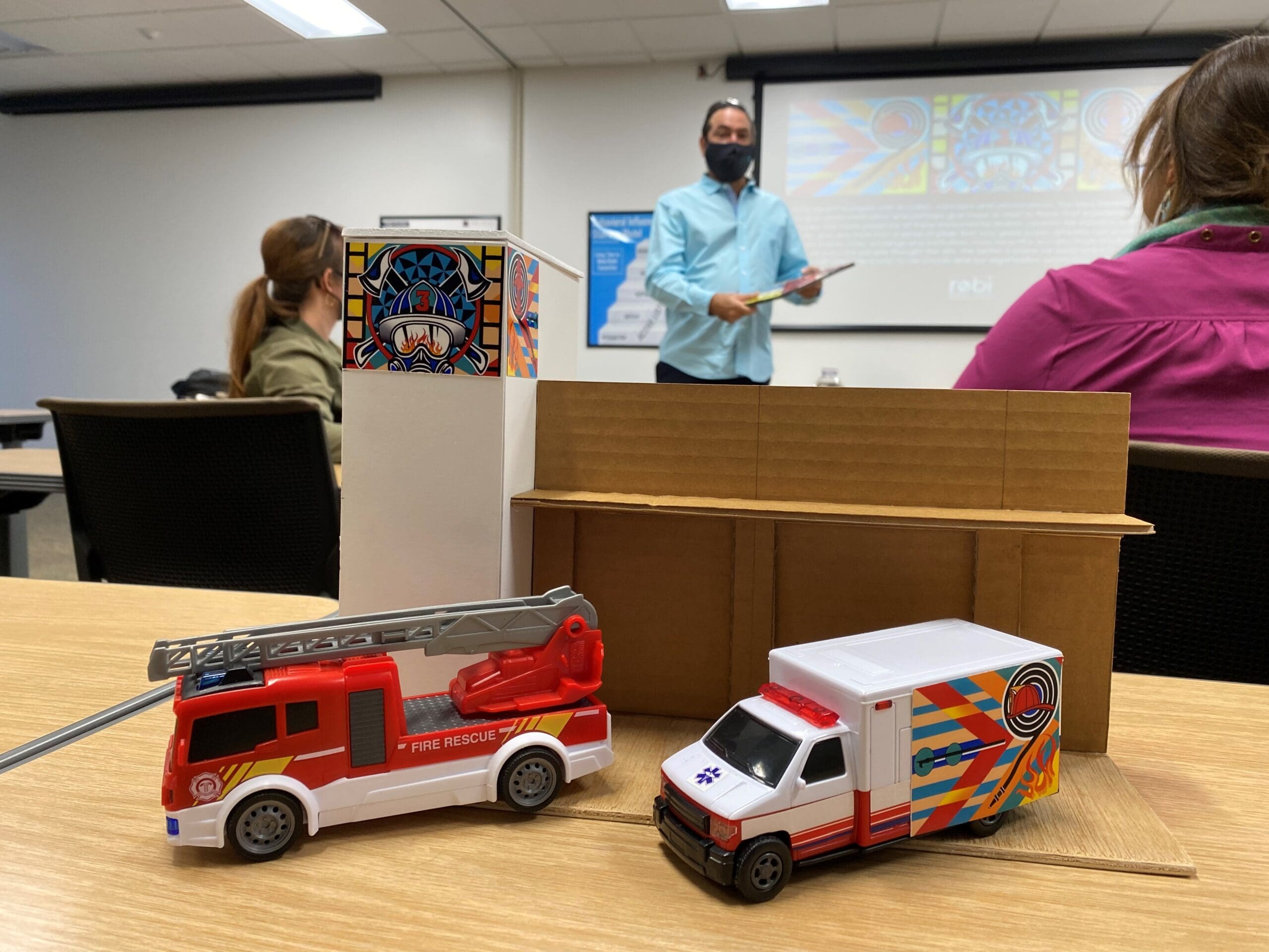 Man standing in front of room with two women looking at his presentation of art concept. 