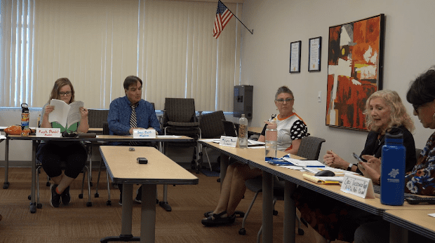 Five people sitting at tables in a meeting.