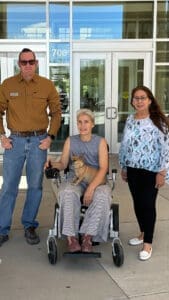 Three people in front of City Hall, One is in a wheelchair with a pup on her lap.