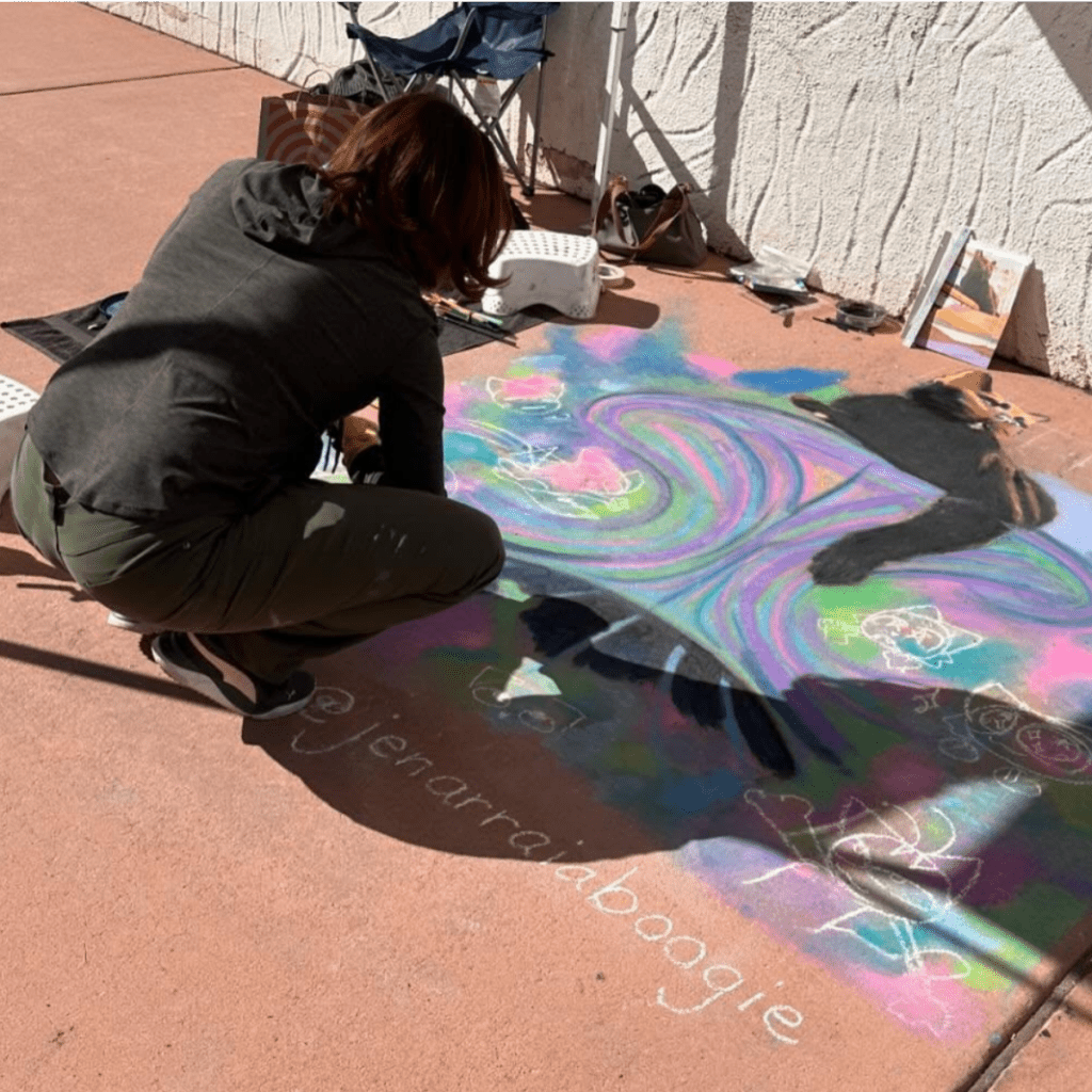 Woman using colored chalks to create art on a sidewalk.