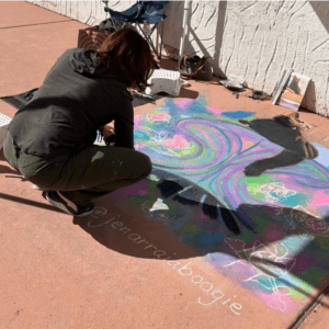 Woman using colored chalks to create art on a sidewalk.