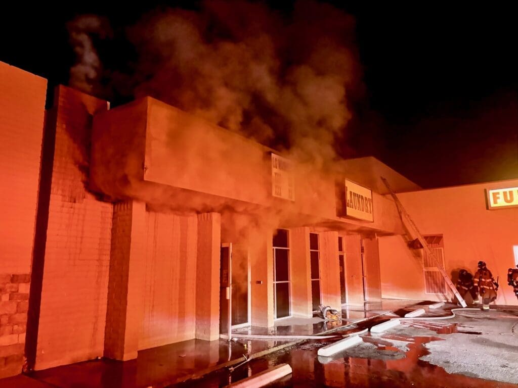 Firefighters standing in front of a business with smoke coming out of the door