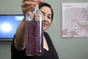 A picture of a woman holding a clear bottle full of swirling purple liquid with glitter inside it.