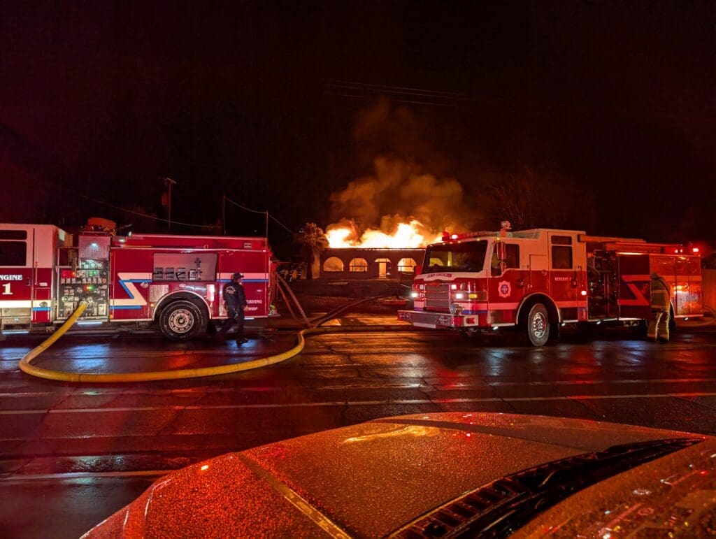 Two fire trucks parked in front of a burning house.
