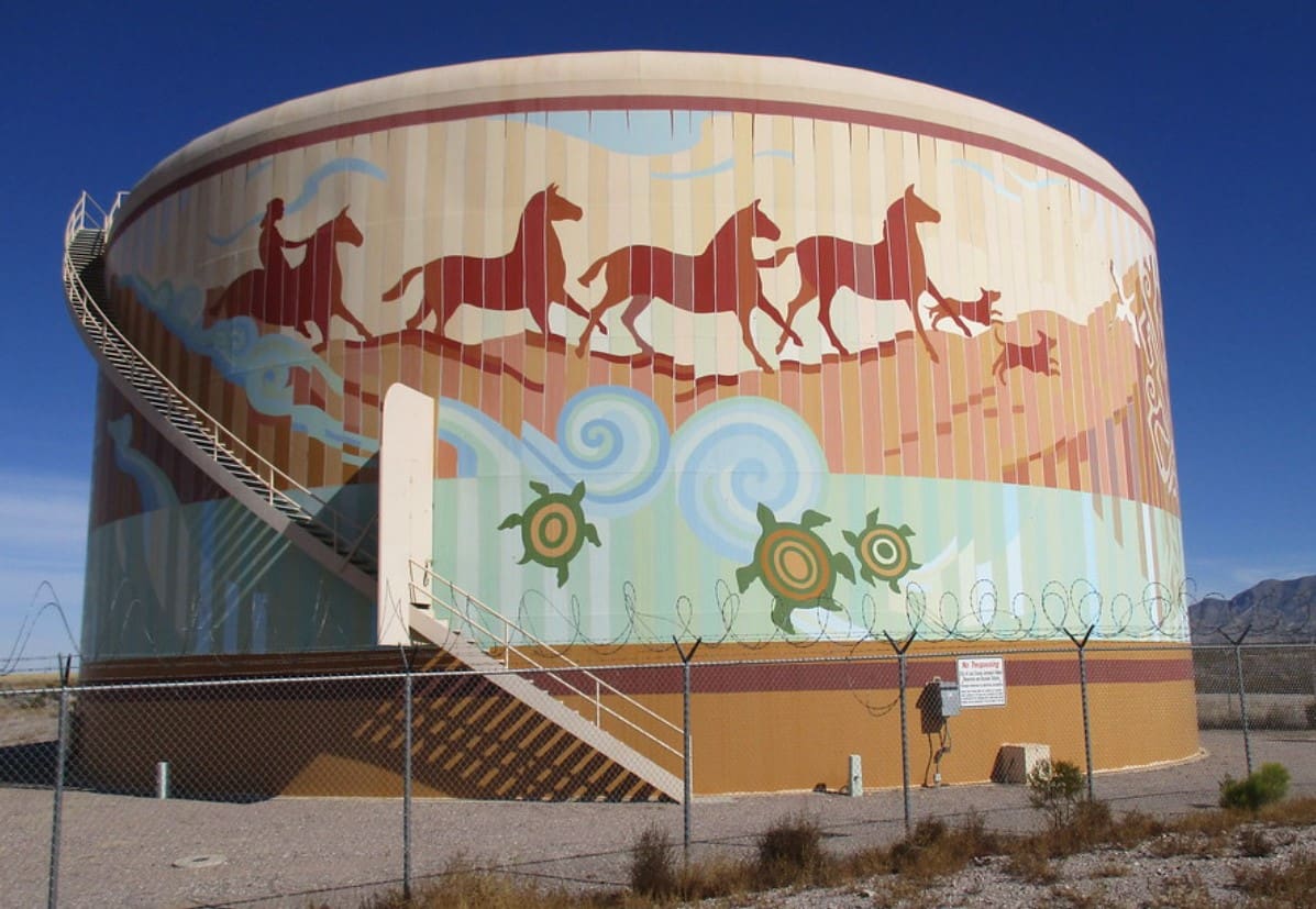 Water tank mural showing indigenous person on a horse driving horses across desert with desert turtles swimming in water.