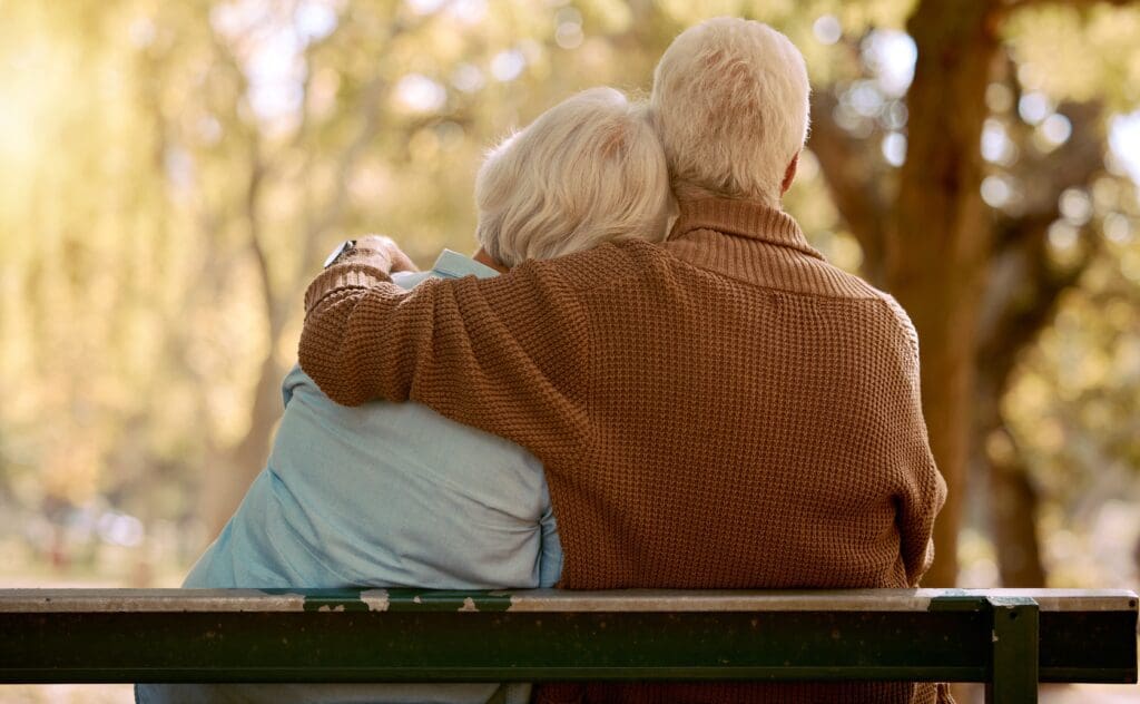 Older man hugging an older woman on a park bench.