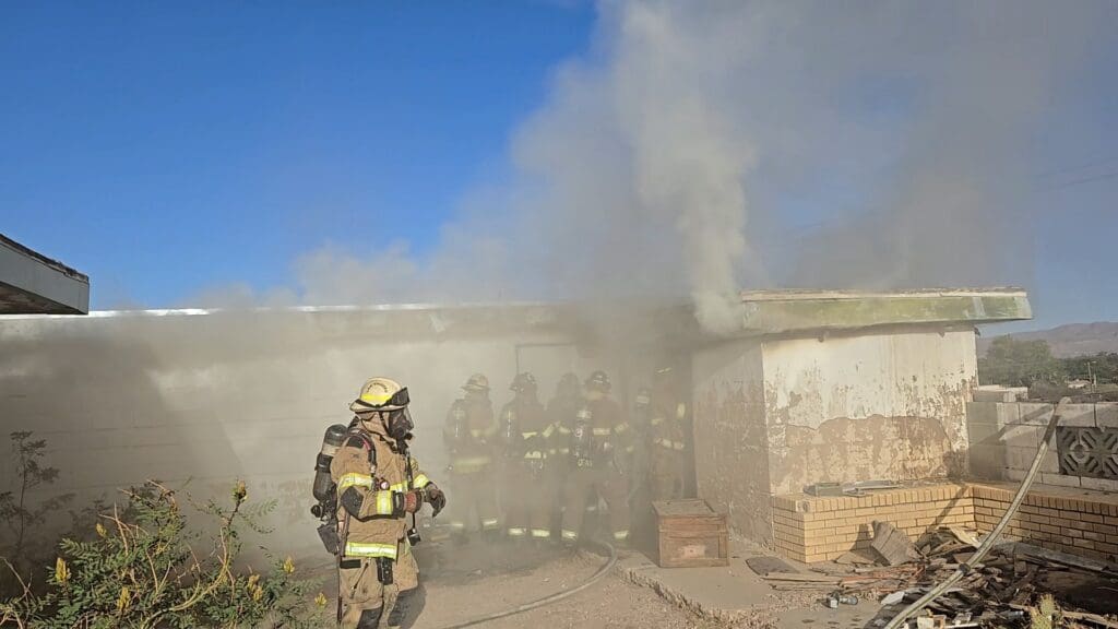 Firefighters entering a house with smoke coming out of it.