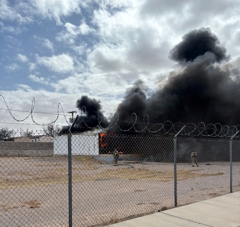 Two firefighters fighting fire with heavy smoke coming out of the building.