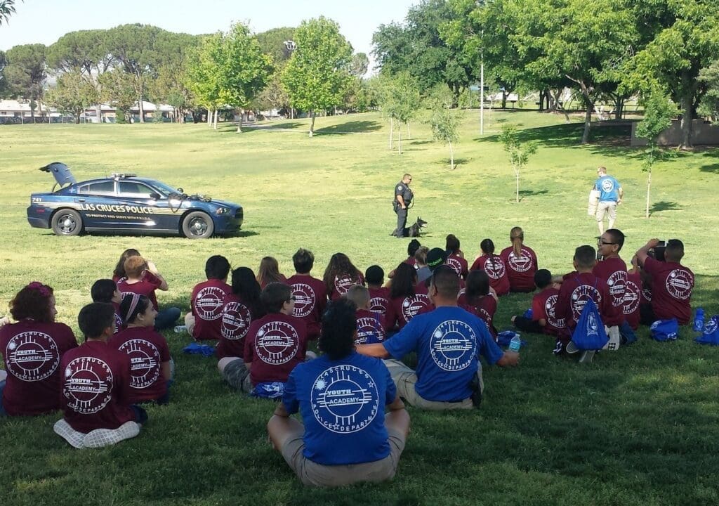A group of children sitting on the grass watching a demonstration by a police officer and his dog,