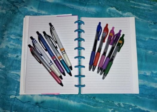 Open notebook with many pens on it.