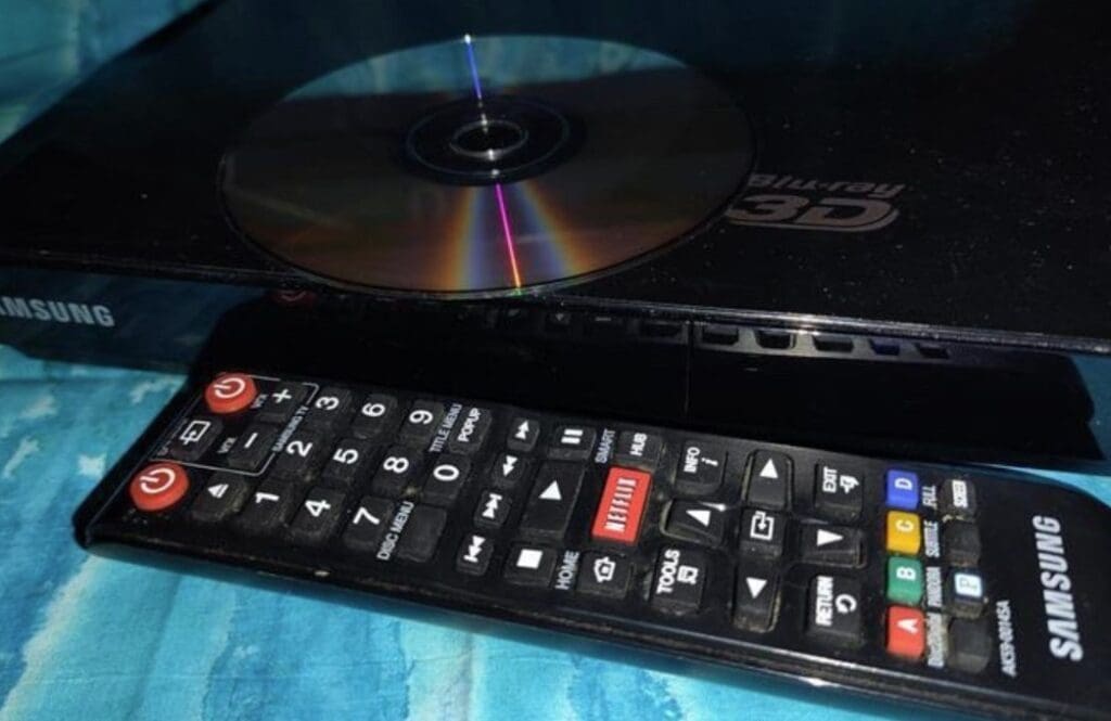 A DVD on top of a DVD player with a remote in front.