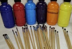 Assorted bottles of paint and paint brushes on a table.