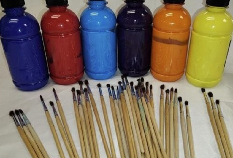 Assorted bottles of paint and paint brushes on a table.