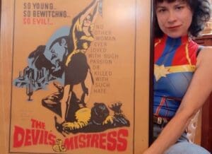 Sitting woman holding a poster for The Devil's Mistress.