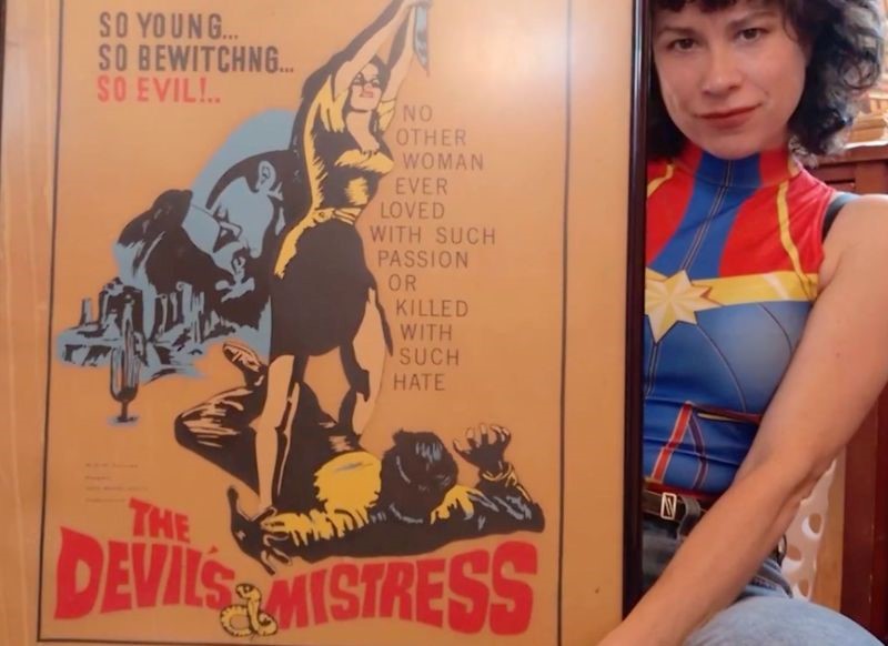 Sitting woman holding a poster for The Devil's Mistress.