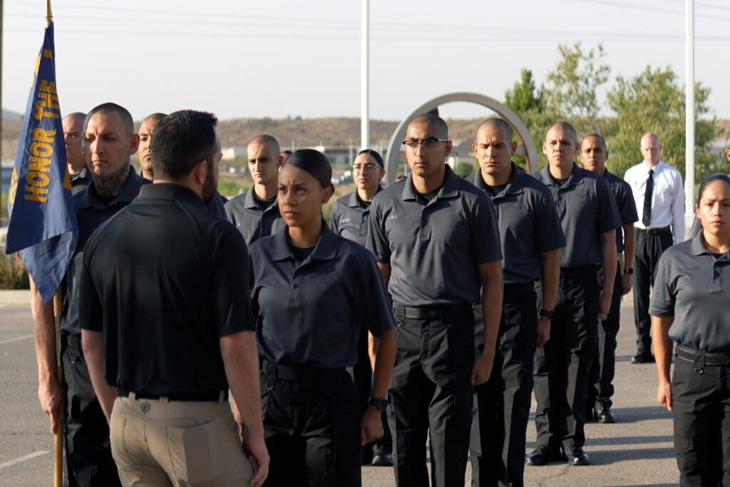A group of recruits standing at attention listening to an instructor.