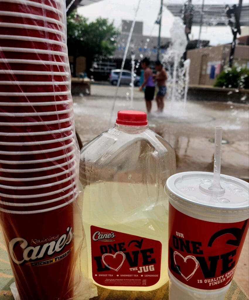 A jug of lemonade with cups from Raising Cane's.