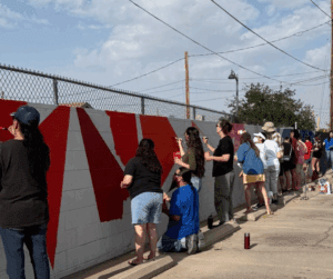 Many people painting a cinder block wall.