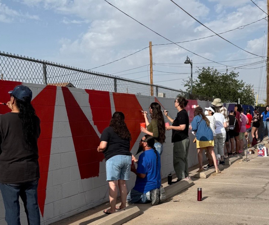 Many people painting a cinder block wall.