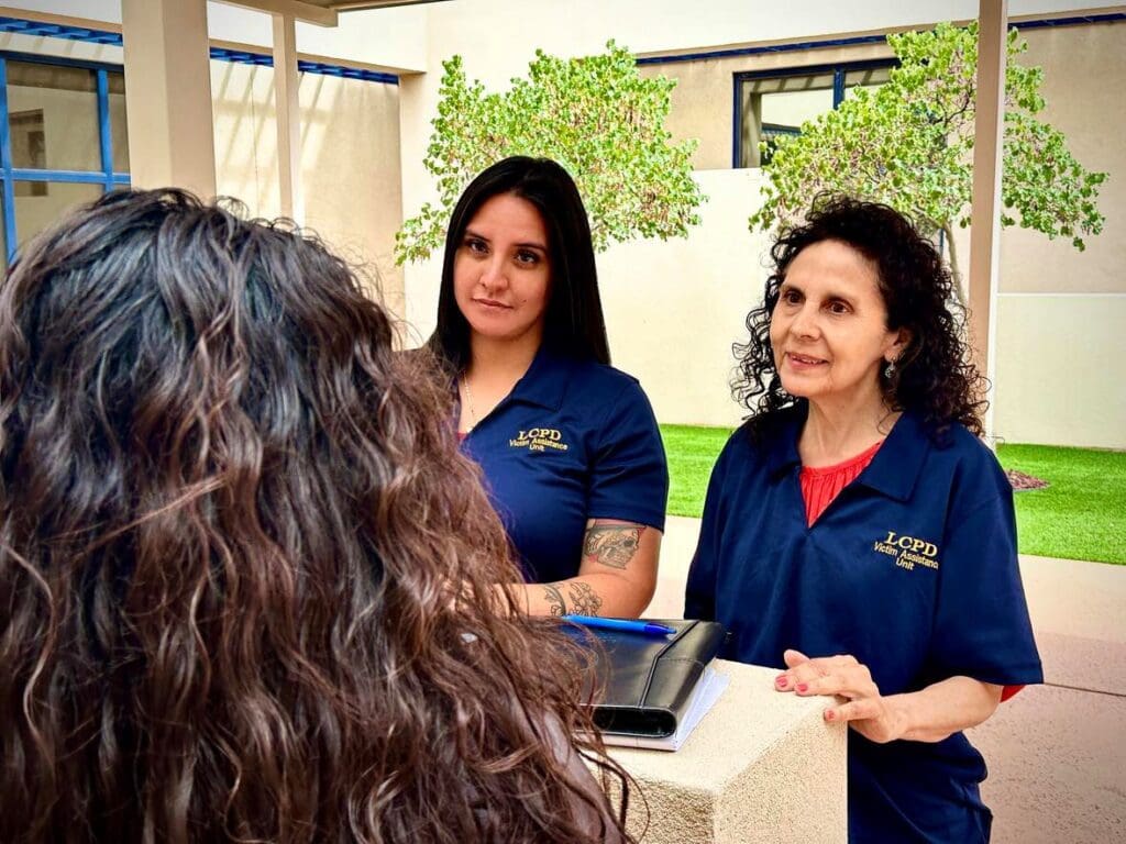 Two women with Las Cruces Police Department Victim Advocate Team shirts talking to another woman.