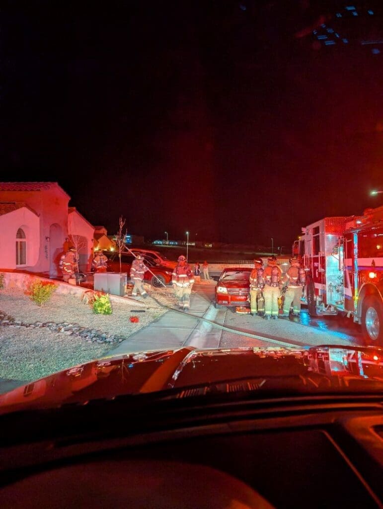 Group of firefighters standing outside of a house with fire engine in the road.
