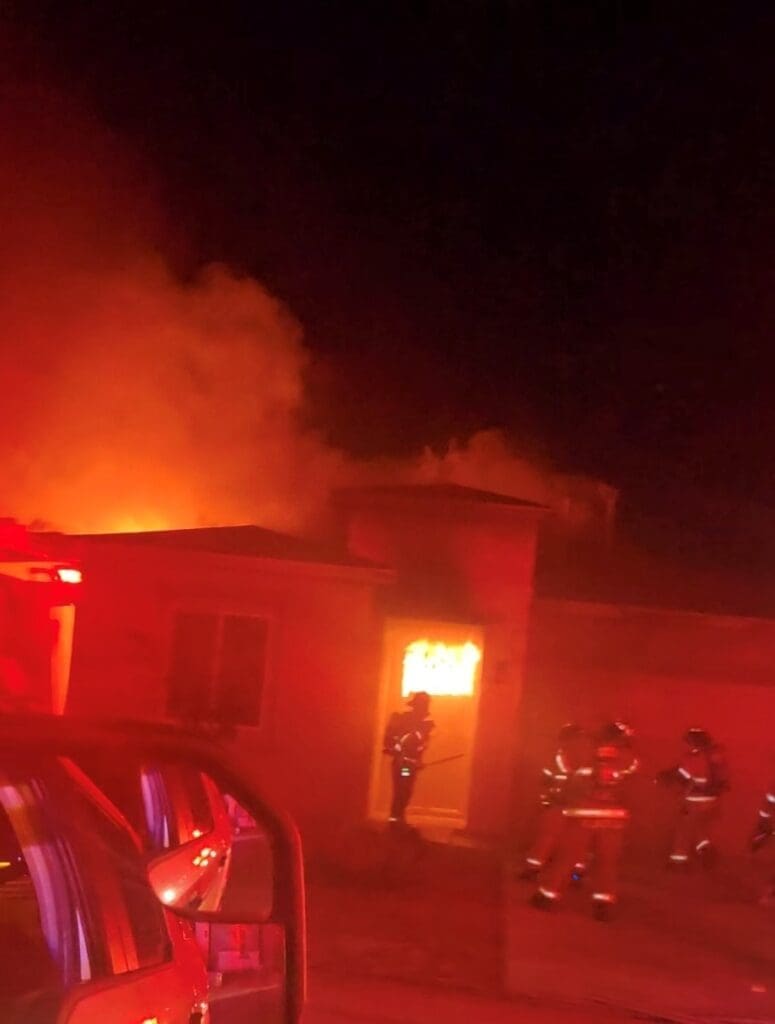 Firefighters standing outside of a burning house.
