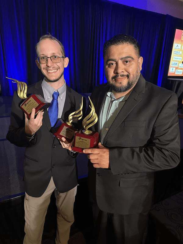 Two men holding up three trophies.