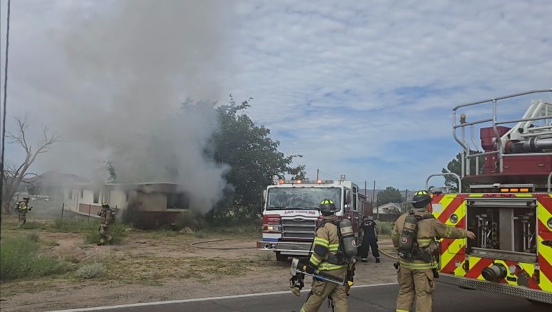 Fire trucks in front of a mobile home that has smoke coming out of it.