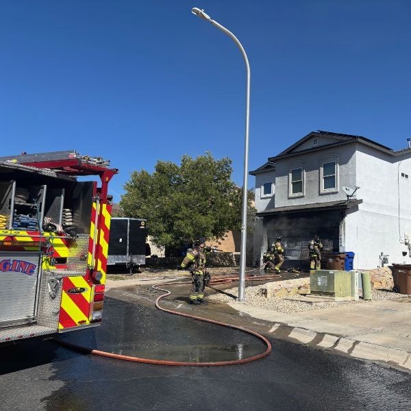 Firefighters in extinguishing a fire at the front of a house with a fire truck parked on the street.