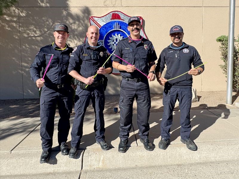 Four firefighters standing on a sidewalk holding glow sticks.