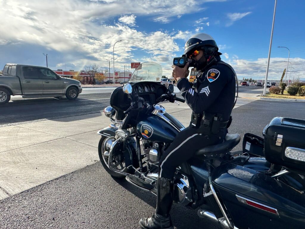 Officer on a motorcycle parked in a parking lot with a radar gun.
