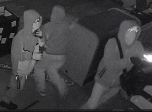 Three individuals in hoodies in a picture taken by surveillance camera.