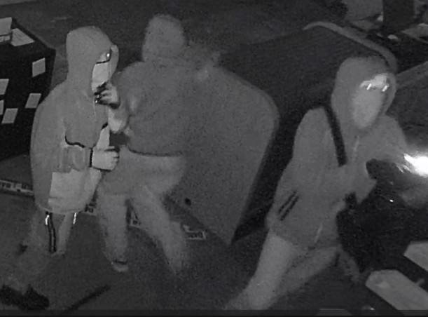 Three individuals in hoodies in a picture taken by surveillance camera.