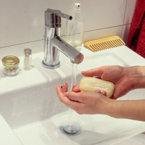 Someone washing their hands under a running faucet holding a bar of soap.