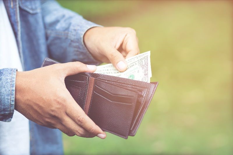 Person holding a wallet with money inside of it.