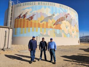 Three utility workers standing in front of a water tank.
