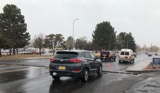 Cars driving on a wet street with light snow falling.