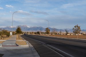 Photo of Mesa Grande Drive in Las Cruces. Vide from the sidewalk showing the road and the trees on the opposite side of the street.