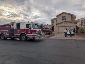 Group of people standing outside of a house, along with a fire truck parked on the road.