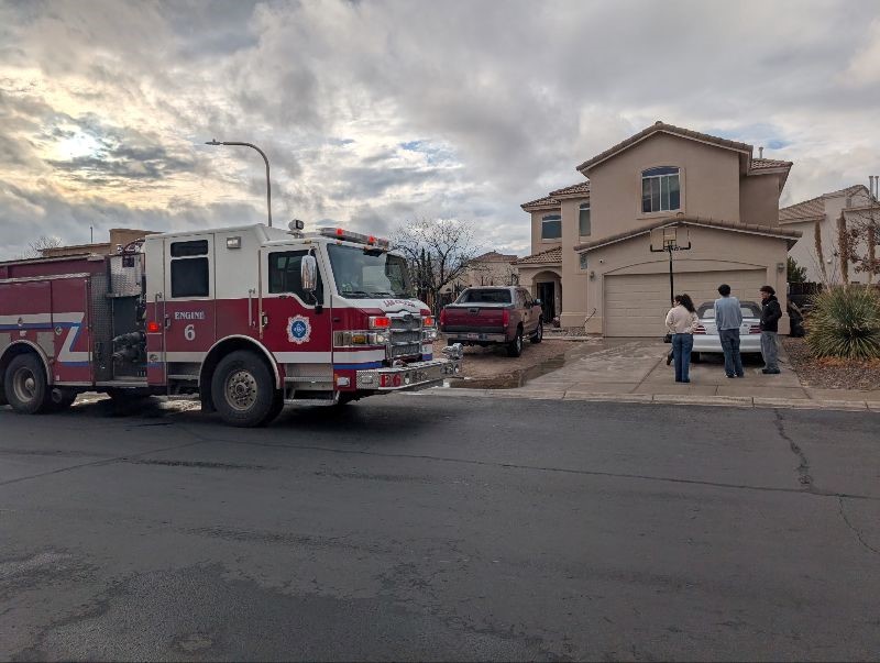 Group of people standing outside of a house, along with a fire truck parked on the road.