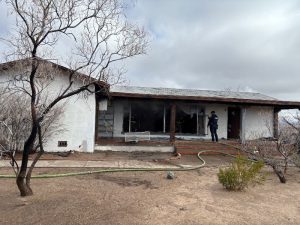 A police officer removing a screen from a window of a home that was damaged by a fire.