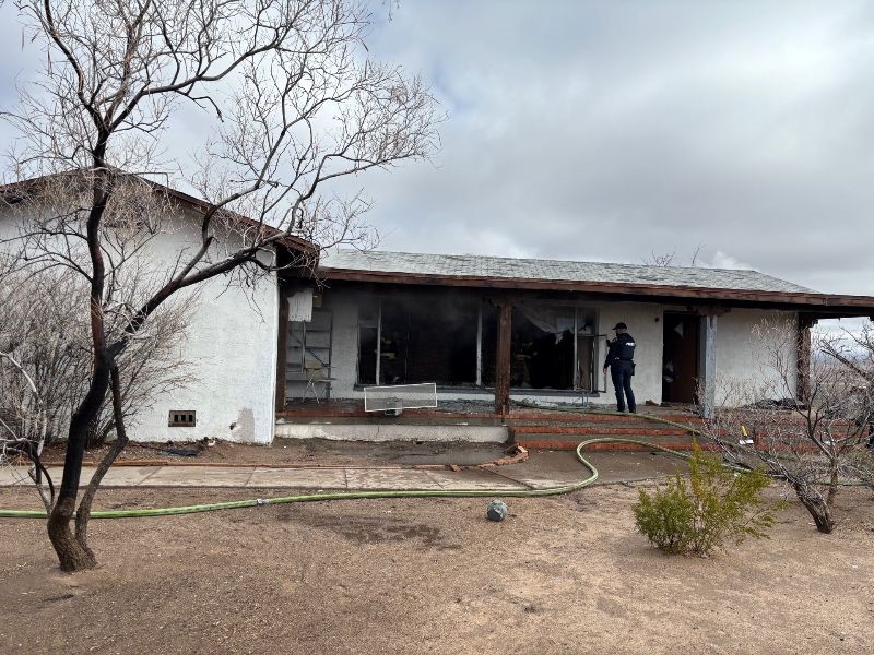 A police officer removing a screen from a window of a home that was damaged by a fire.