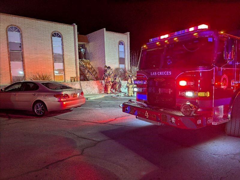 Fire truck parked in apartment complex parking lot with a group of firefighters standing outside the building.