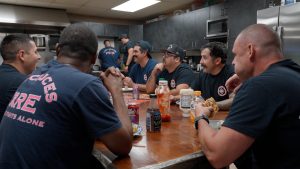 Firefighters sitting at a table eating food and having a discussion.