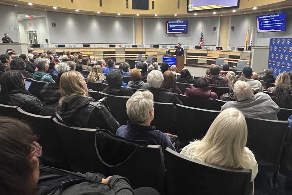 People seated in City Council Chambers listening to a speaker.