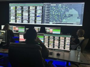 Real Time Crime Center tv monitors with data being displayed and people sitting at desks overlooking the data.