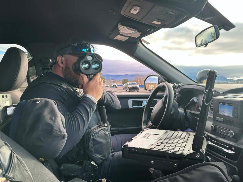 An officer points a radar gun while sitting in his vehicle.